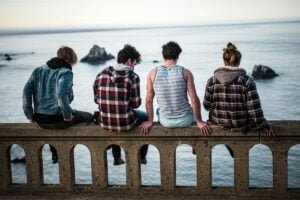 Image of 4 people sitting on a ledge looking over the sea with small islands